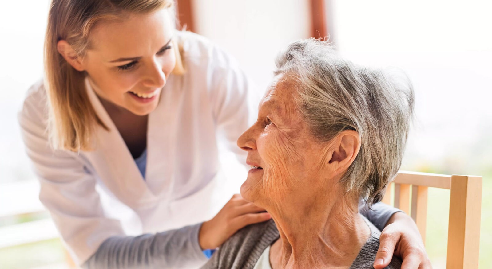 Young woman in white coat, presumably a doctor, talking to old woman, both smiling.