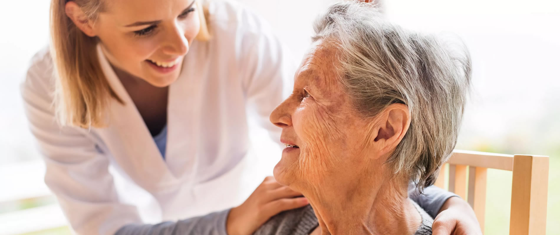 Young woman in white coat, presumably a doctor, talking to old woman, both smiling.