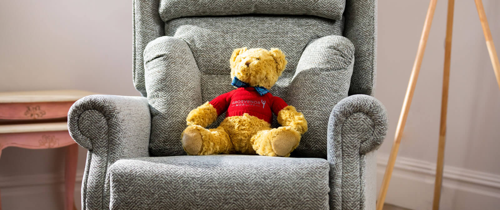 A brown fluffy bear sitting on a grey armchair.